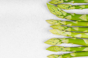 Bunch of raw fresh green asparagus stalks macro, close up on light gray textured background with...