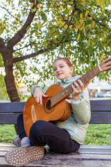 Teen girl playing guitar outdoors in autumn