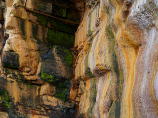 The textured cliff shows colorful mineral layers and patches of green moss