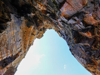 Rocky cliffs form a natural arch with a view of the bright blue sky
