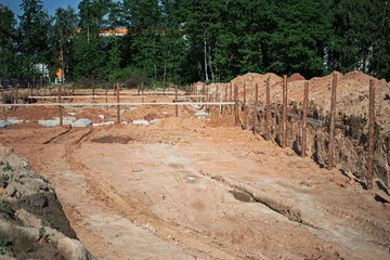 Construction site with freshly dug foundation surrounded by wooden supports and sand on a sunny day
