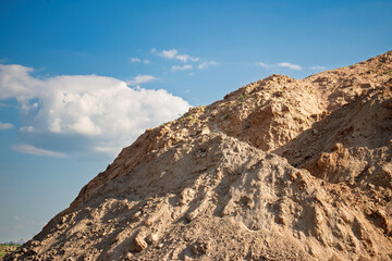 Construction site with a large mound of soil under a bright blue sky during daylight hours