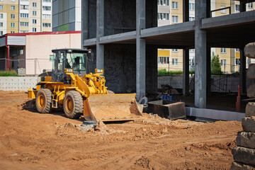 Construction machinery operates at a building site during bright afternoon in a residential area