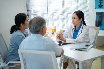 Asian woman Doctor Explaining Prescription Medication to Senior Patients.asian doctor discusses medication instructions while holding a prescription bottle,attentively guiding couple elderly patients