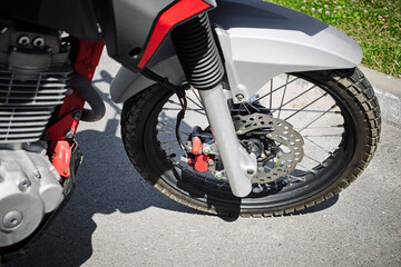 Close view of motorcycle front wheel showing disc brake system in outdoor setting at bright daytime