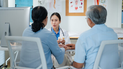 Asian woman Doctor Explaining Prescription Medication to Senior Patients.asian doctor discusses medication instructions while holding a prescription bottle,attentively guiding couple elderly patients
