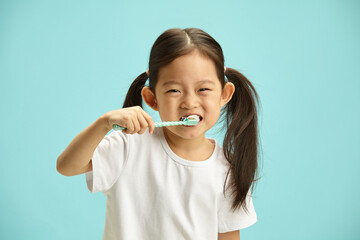 Studio photo of happy cheerful girl kid with brunette ponytail hair brushing her teeth, taking care...