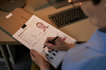 Middle aged Caucasian woman holding clipboard reviewing criminal profile document with mugshot and...