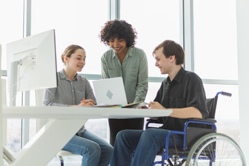 Teamwork brainstorm. Diverse multiracial colleagues man in chair for people with disability working together. Group of people sitting in creative office discussing business. Young professional team