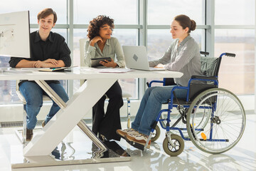 Teamwork brainstorm. Diverse multiracial colleagues woman in chair for people with disability working together. Group of people sitting in creative office discussing business. Young professional team