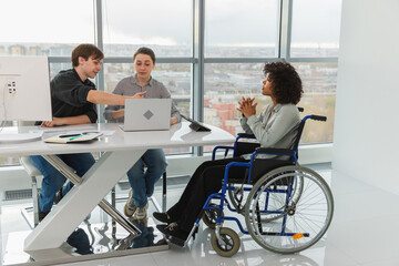 Teamwork brainstorm. Diverse multiracial colleagues woman in chair for people with disability working together. Group of people sitting in creative office discussing business. Young professional team