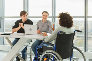 Teamwork brainstorm. Diverse multiracial colleagues woman in chair for people with disability working together. Group of people sitting in creative office discussing business. Young professional team