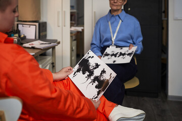 Young adult Caucasian woman wearing orange prison uniform, sitting in office holding inkblot test...