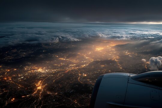 Night view of a city glowing under clouds from an airplane window during twilight - Powered by Adobe