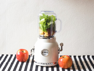 Front view of  white vintage blender or smoothie maker machine  with an apple on  black and white stripe table cloth and white wall. Healthy drink making.