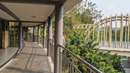  A modern curved walkway with a metal railing and grey columns, leading to a unique arched bridge...