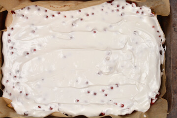 White meringue topping over a red currant cake in a parchment-lined baking tray, seen from above