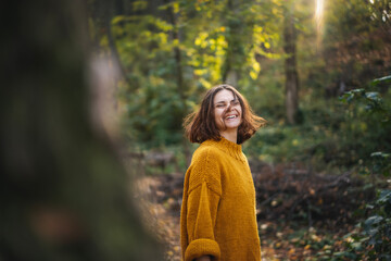 Smiling young woman with curly hairstyle enjoying the autumn nature in the forest