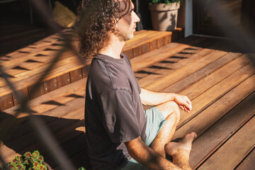 Young man doing morning yoga on wooden patio in country cottage in summer