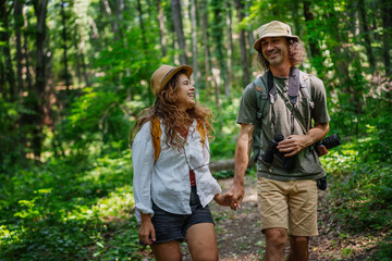 Young happy couple hiking in summer forest holding hands