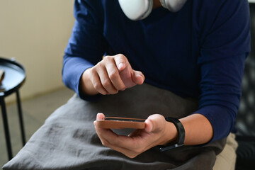 A man is sitting on a couch, holding a cell phone in his hands and looking at it intently. He is focused on the screen, possibly checking his messages or browsing the internet.