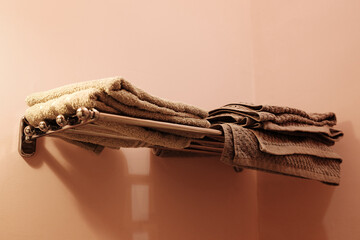 Stack of folded brown towels on a chrome wall-mounted rack in a bathroom with soft pink walls....