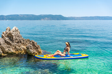 Woman relaxing on SUP board by rocky shore