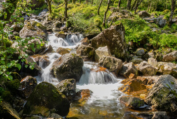 Slow shutter smooth water waterfall over rocks in the sunshine, Glen Nevis