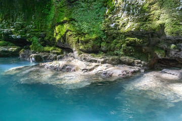 Emerald turquoise water pool in limestone cave canyon with moss walls