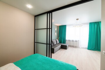 modern room featuring a turquoise bedspread, frosted glass sliding doors with a black frame, and a cozy living area with turquoise curtains