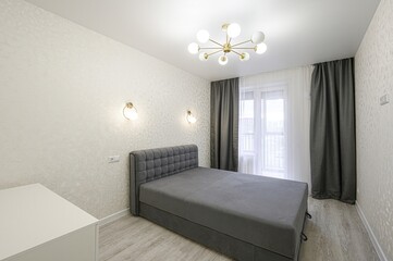 modern bedroom with a gray bed, textured wallpaper, and stylish lighting fixtures. Curtains frame a bright window