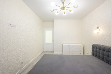 Bright bedroom featuring a gray bed, white dresser, patterned walls, a modern ceiling light, and a...