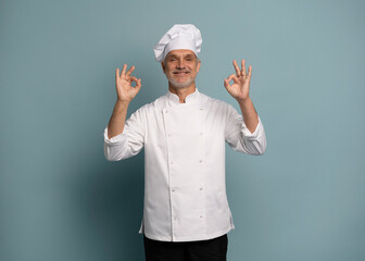 Portrait of a smiling male chef cook showing ok sign isolated on blue background.