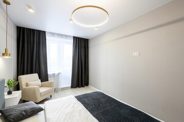 modern bedroom features a bed, armchair, dark curtains, and a striking circular ceiling light....