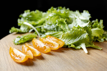 Close-up of tomatoes and lettuce on a wooden board on a black background. Concept of healthy eating and organic farm products