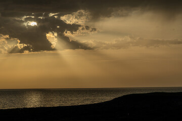 Dark storm clouds with golden sunlight breaking through over calm ocean water