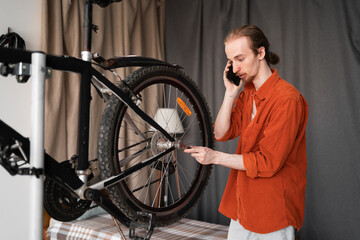 young man talking on mobile phone while fixing a bike in home interior