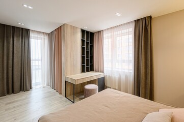 warmly lit bedroom features a neatly made bed and a desk built into a shelving unit, all framed by...