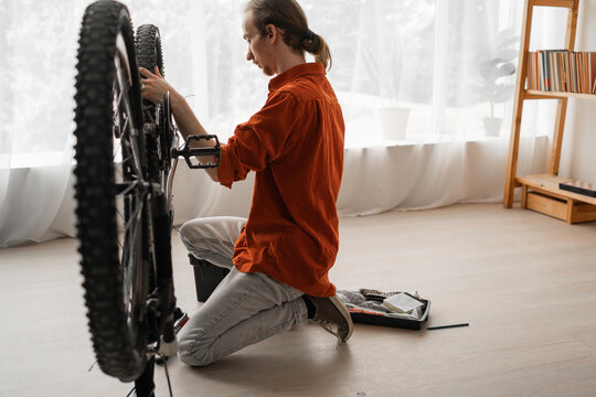 Focused man inspects and repairing a bike bicycle in apartment interiors - Powered by Adobe