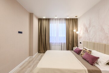 Cozy bedroom with beige bed, brown curtains, and floral wallpaper. Soft lighting creates a warm and inviting ambiance