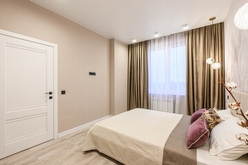 modern bedroom with a neutral palette featuring a bed, a window with curtains, a white door, and simple decor