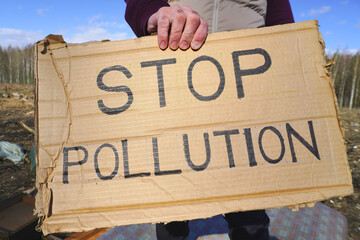 Activist showing stop pollution sign at landfill site during sunny day