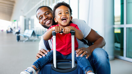 Smiling afro-american dad and cute happy boy sitting on the suitcase at airport. travel, adventure, vacation, little tourist, tickets sale, last minute flight, suitcase mood, holiday vibes