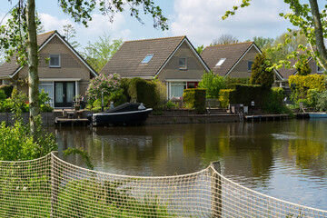 Several nice houses are standing in a row in the Netherlands near the small summer river. One typical summer day in the Netherlands on the street near the canal