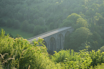 Stone bridge over lush forested valley at golden hour light, ideal outdoor location for walking or...