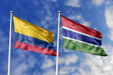 Colombia and Gambia flags majestically unfurling against a vivid blue sky, symbolizing...