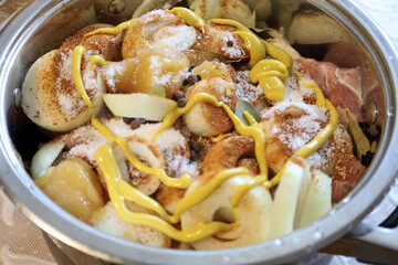 In a pot, pieces of meat, onions, spices, bay leaves, and mustard are being prepared, creating a...