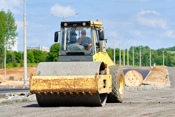 Yellow single drum roller machine parked on construction site, suburban road development, preparing...