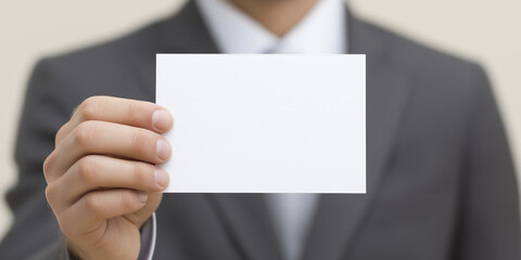 Fototapeta premium Businessman in formal suit holding blank white card in front of him, showcasing a clean and professional appearance, ideal for advertising or promotional use