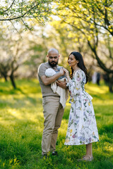 Fototapeta premium In a picturesque park, a man and a woman are lovingly holding a baby